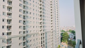 A high-rise residential building with multiple balconies and a view of a swimming pool and surrounding greenery. - Comfortable And Modern 2Br At Grand Palace Kemayoran Apartment (Jakarta)