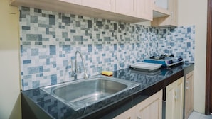 A kitchen with a tiled backsplash, a stainless steel sink, and wooden cabinets. - Comfortable And Modern 2Br At Grand Palace Kemayoran Apartment (Jakarta)