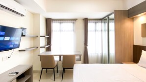 Une chambre d’hôtel avec un lit, un bureau avec deux chaises, une télévision et une fenêtre avec des rideaux.