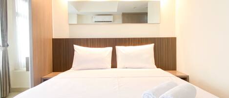 A hotel room with a large bed, two white pillows, a wooden headboard, and a mirror above the bed.