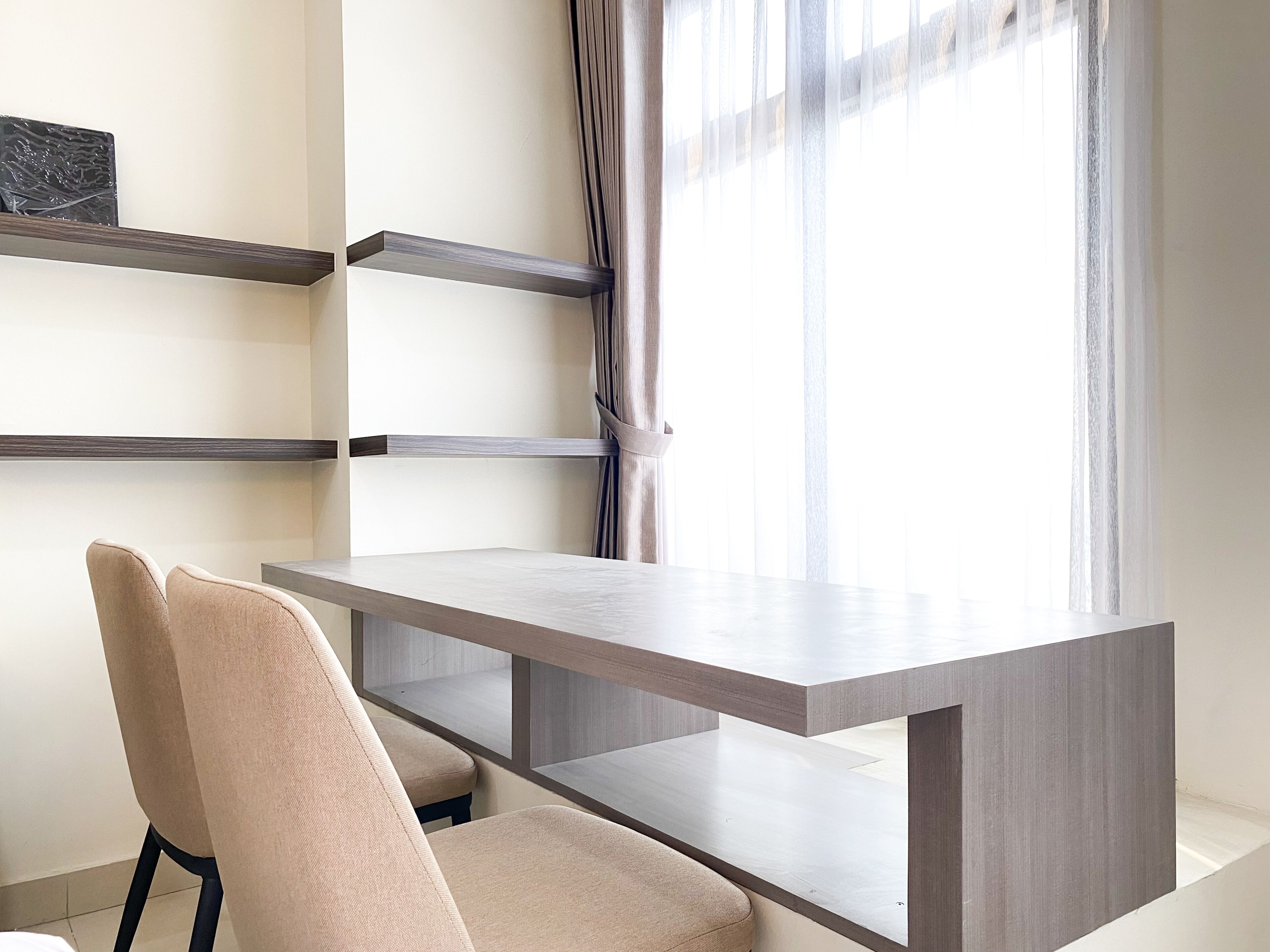 Una habitación moderna con un escritorio minimalista, una silla y un ventanal con cortinas traslúcidas.