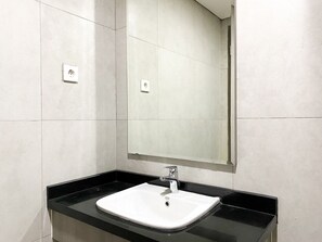 Un baño con lavamanos blanco, encimera negra y un espejo sobre el lavamanos.