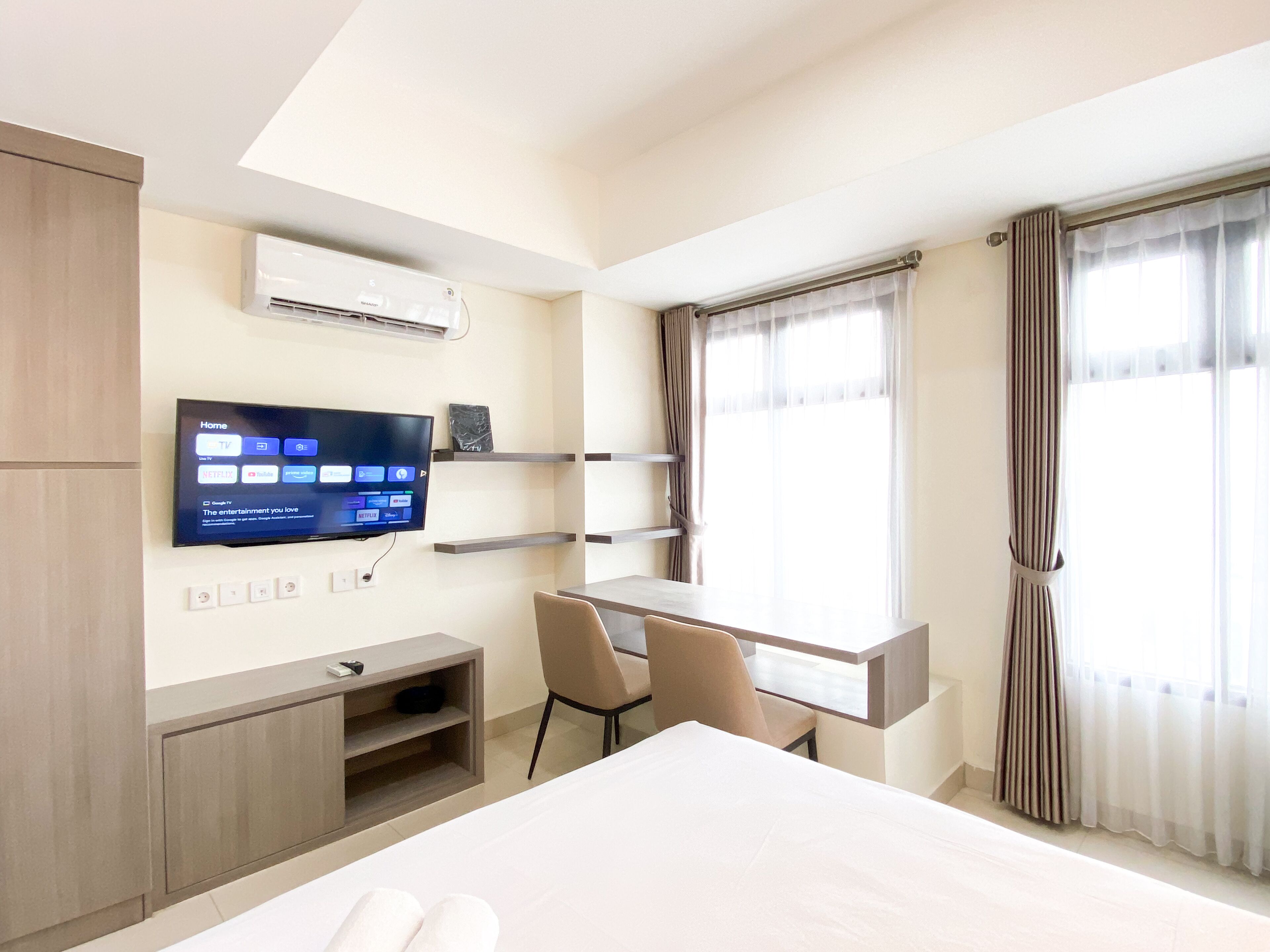 Une chambre d’hôtel comprenant un lit, un bureau avec une chaise, un téléviseur à écran plat fixé au mur et une fenêtre avec des rideaux.