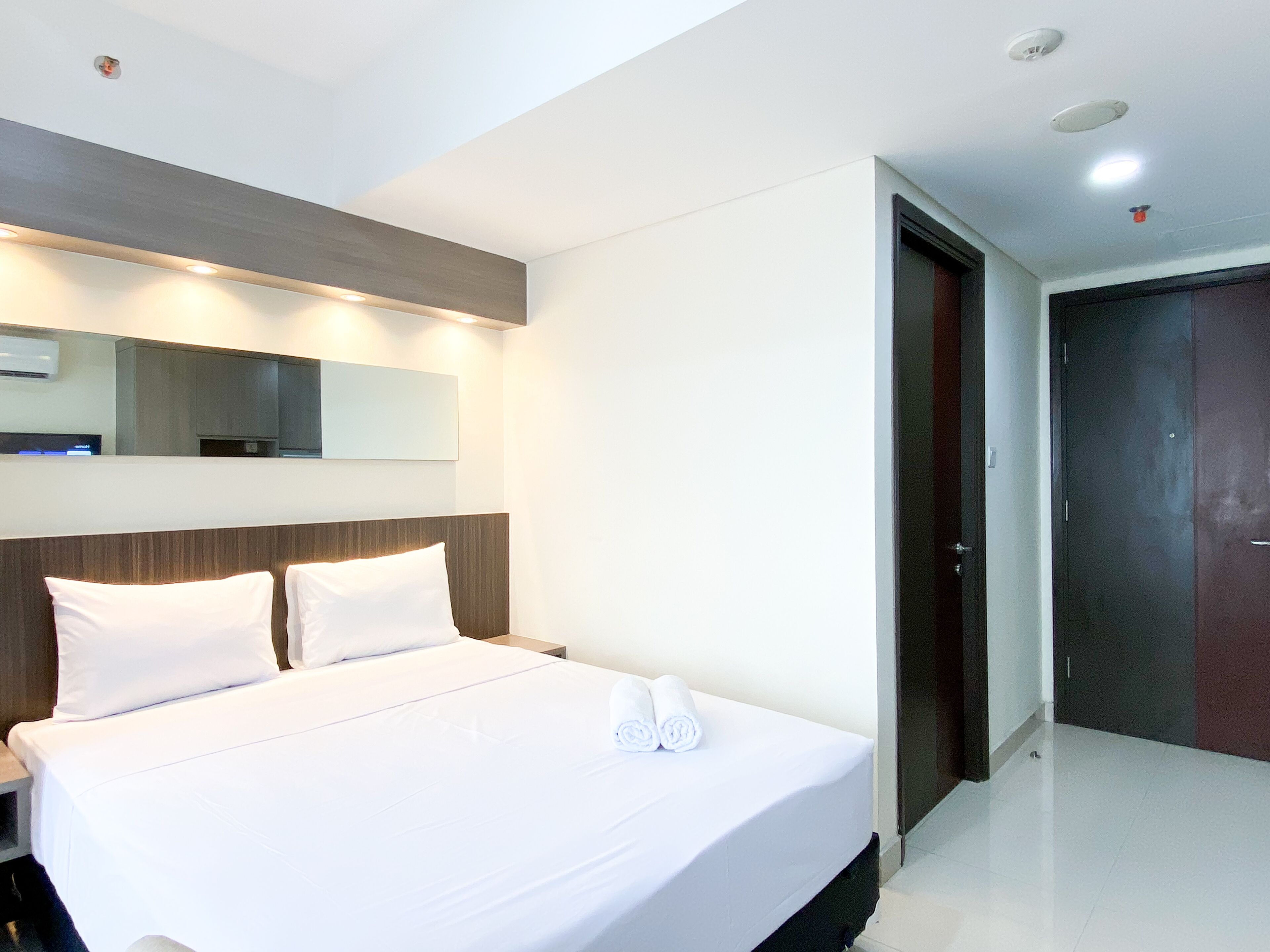 A hotel room with a large bed, a nightstand, a mirror, and a door.