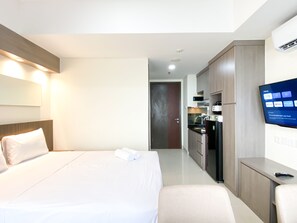 Una habitación de hotel con cama, escritorio, televisión y kitchenette.