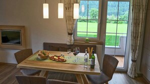 A dining area with a wooden table set for four, a television on the wall, and a view of a green landscape through the window. - Chalet in Mayrhofen near Penkenbahn Ski Lift (Mayrhofen)