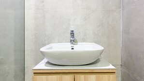 A bathroom with a white vessel sink on a wooden vanity, tiled walls, and a standard shower.
