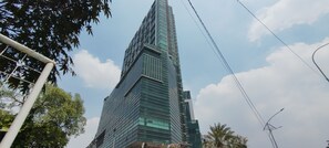 A tall, modern skyscraper with a sleek glass facade and a unique angular design. - Homey 1Br Apartment At Aryaduta Residence Surabaya (Surabaya)