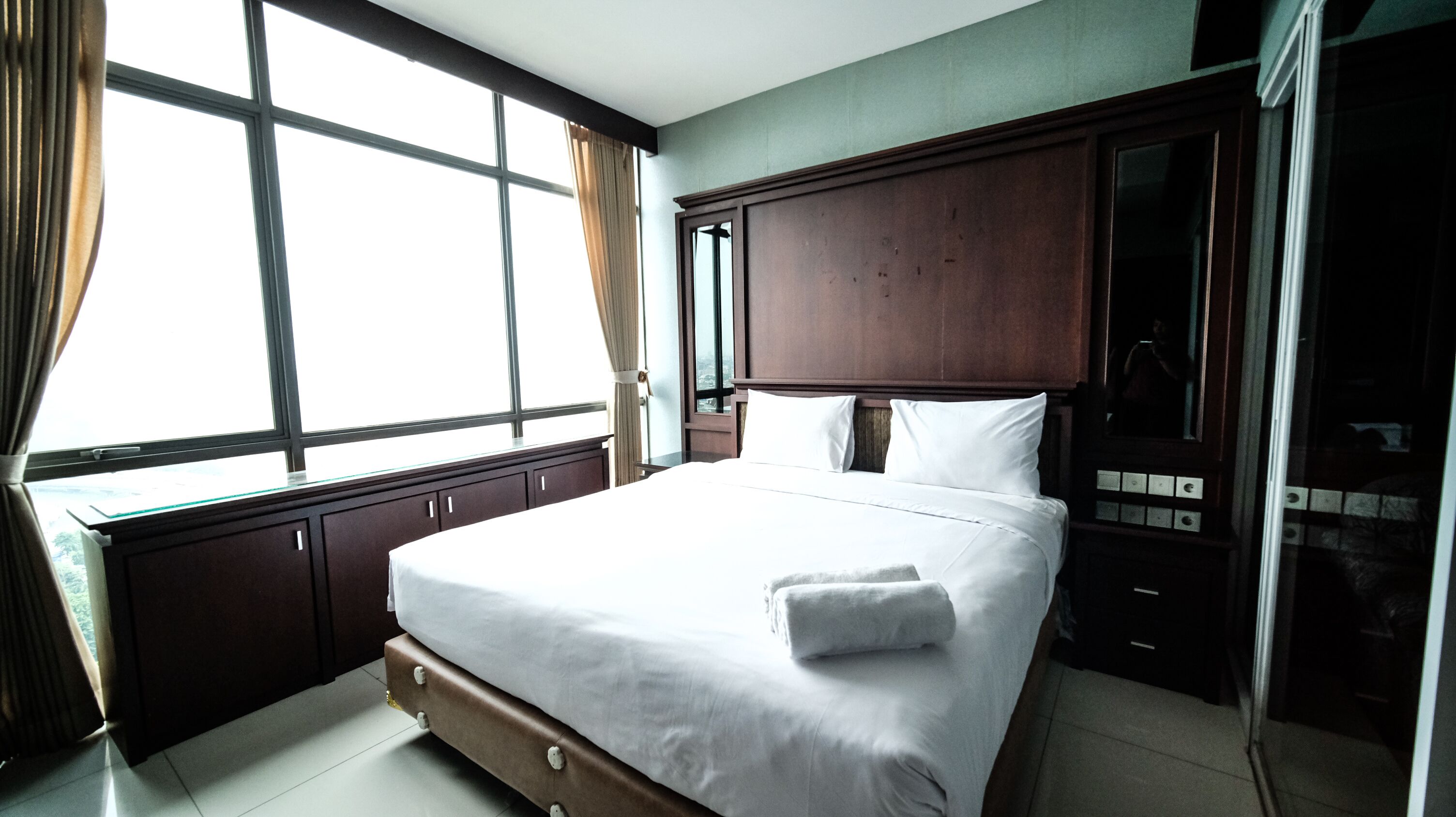 A hotel room with a large bed, wooden headboard, and a view through the window.