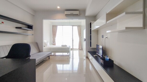 A modern hotel room with a bed, a desk, a chair, a TV, and a large window. - Nice And Comfy 1Br At Dago Suites Apartment (Bandung)