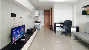 A modern, well-lit room with a flat-screen TV on a black stand, a desk with a chair, and a sofa. - Nice And Comfy 1Br At Dago Suites Apartment (Bandung)