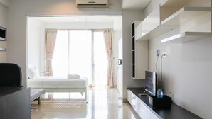 A modern hotel room with a bed, a desk, a flat-screen TV, and a minibar. - Nice And Comfy 1Br At Dago Suites Apartment (Bandung)