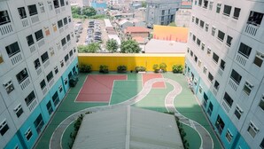 A multi-story building with a basketball court on the ground floor, surrounded by other buildings. - Good Deal And Nice Studio Green Pramuka City Apartment (Jakarta)
