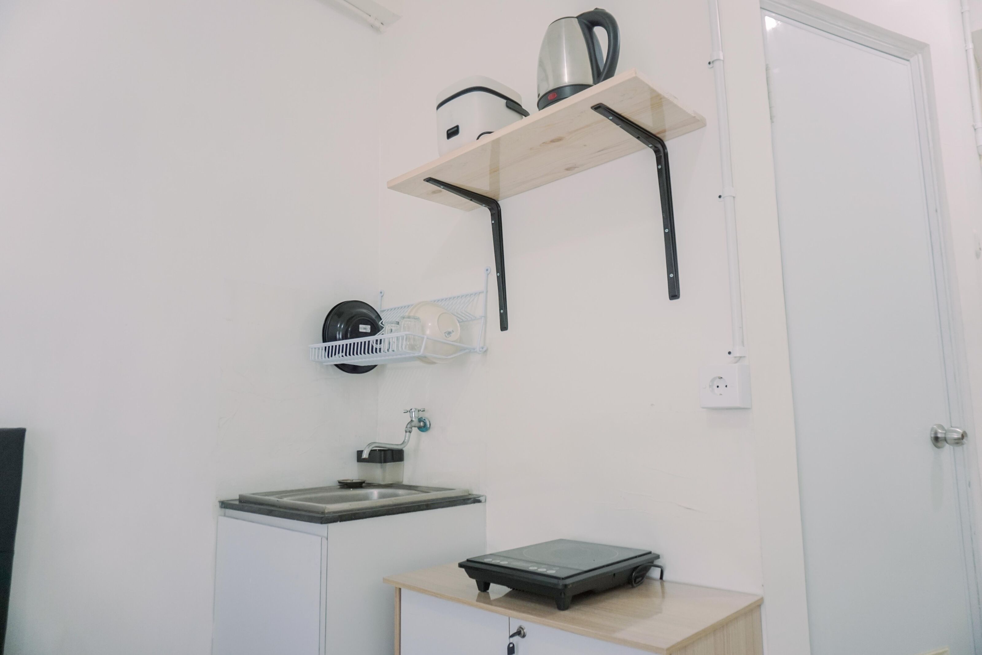 A kitchen with a countertop, a kettle, a coffee maker, a scale, and a hanging rack.