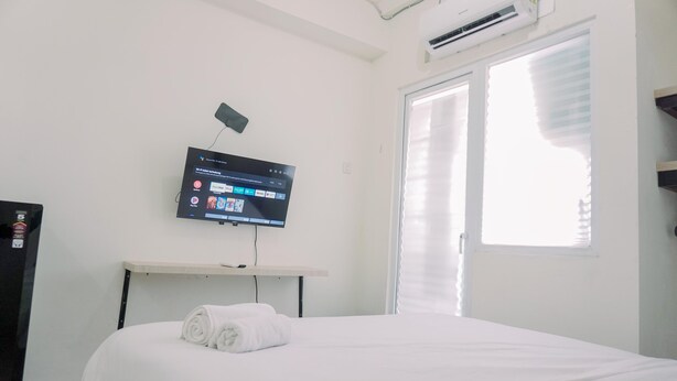 A hotel room with a bed, a TV mounted on the wall, and a window with blinds. - Good Deal And Nice Studio Green Pramuka City Apartment (Jakarta)