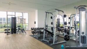 Une salle de sport équipée de divers appareils de musculation, dotée de grandes fenêtres et d’un plancher en bois.