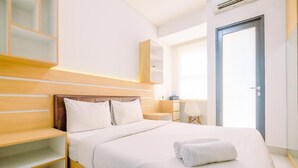A modern hotel room with a wooden headboard, a large bed with white linens, a bedside table with a lamp, and a wardrobe.