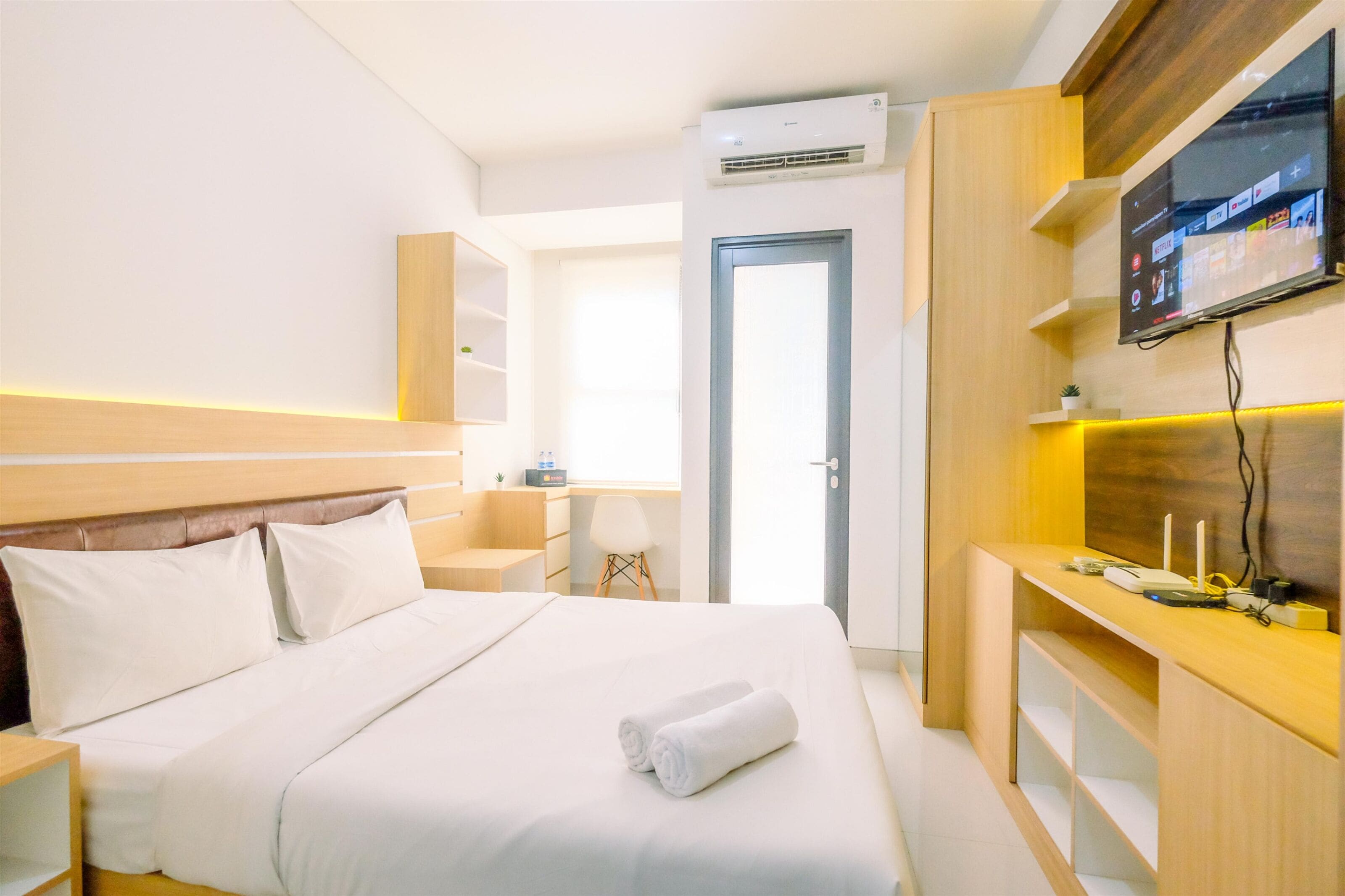 Una habitación de hotel con cama, mesita de noche, televisor y escritorio con computadora.