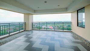 A spacious balcony with a tiled floor and a railing, overlooking a cityscape.
