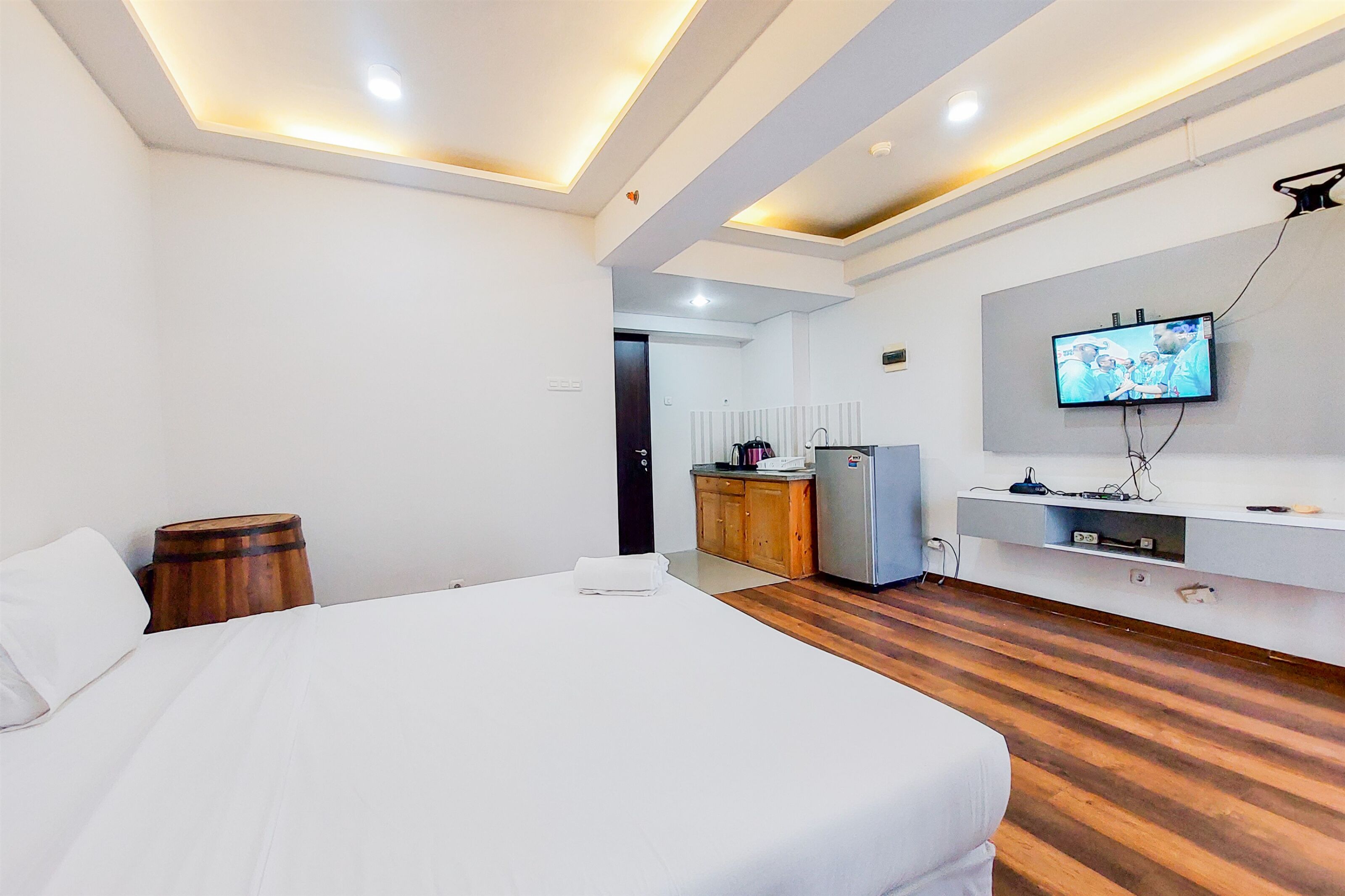 Ein Hotelzimmer mit einem großen Bett, Holzboden, einer Küchenzeile und einem an der Wand montierten Fernseher.