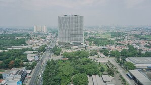 Un immeuble de grande hauteur au design moderne, entouré d’un mélange de bâtiments résidentiels et commerciaux, avec une route au premier plan.