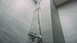 Une douche équipée d’un pommeau de douche à main et d’un robinet mural, dans une salle de bain carrelée.