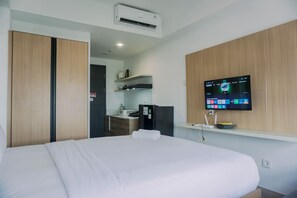 A hotel room with a bed, a TV mounted on the wall, a kitchenette, and an air conditioning unit. - Well Furnished And Comfy Studio Collins Boulevard Apartment (Tangerang)