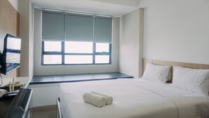 Une chambre d’hôtel avec un grand lit, un téléviseur posé sur un meuble et une fenêtre équipée de stores.