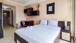 A hotel room with a large bed, a desk with a chair, a small table, and a nightstand with drawers. - Cozy Studio At Galeri Cimbuleuit 1 Apartment (Bandung)