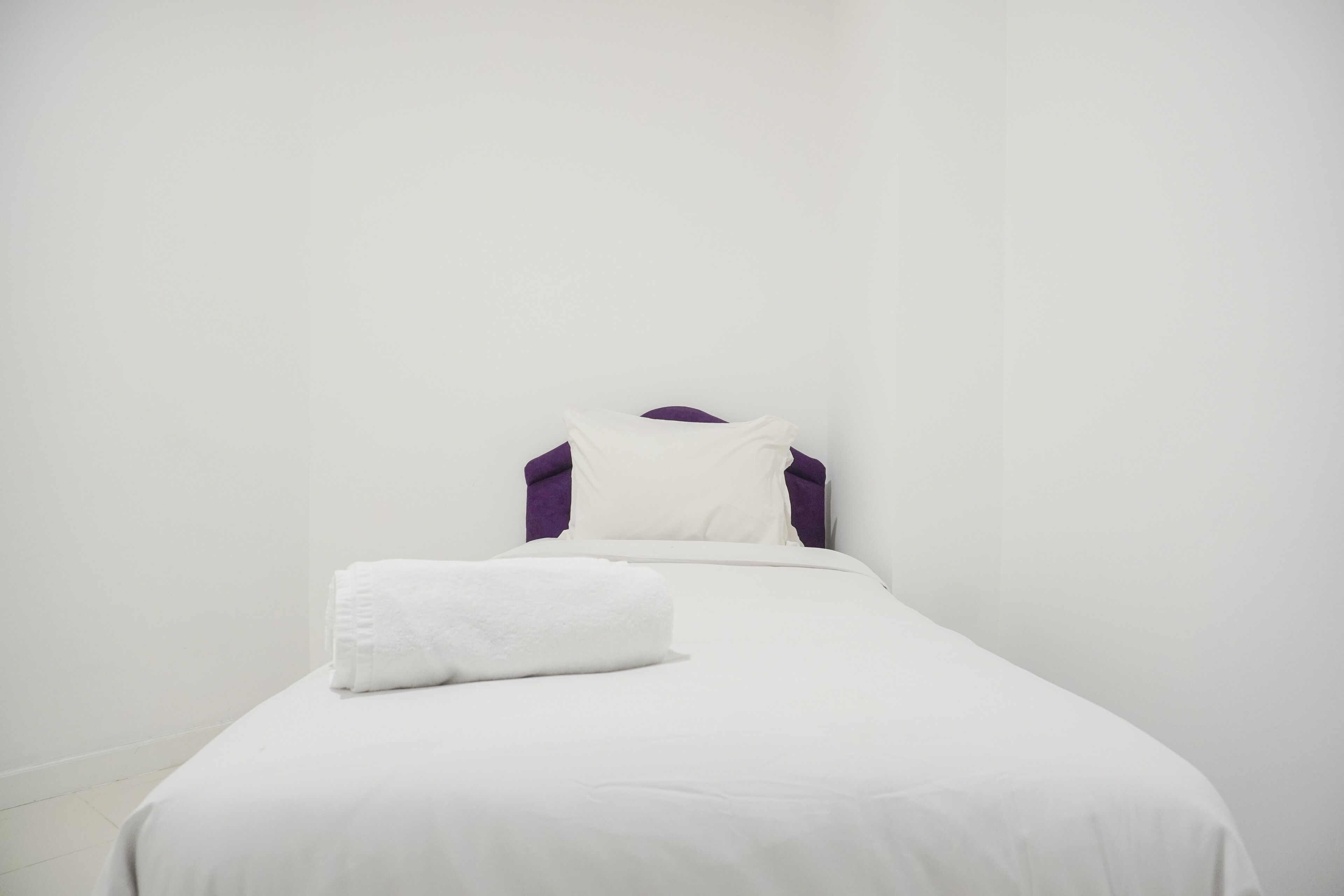 Una cama individual con ropa de cama blanca y una almohada blanca.