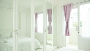 Une chambre dotée d’un grand miroir, d’un lit avec du linge de lit blanc et d’une porte-fenêtre coulissante donnant sur un balcon.
