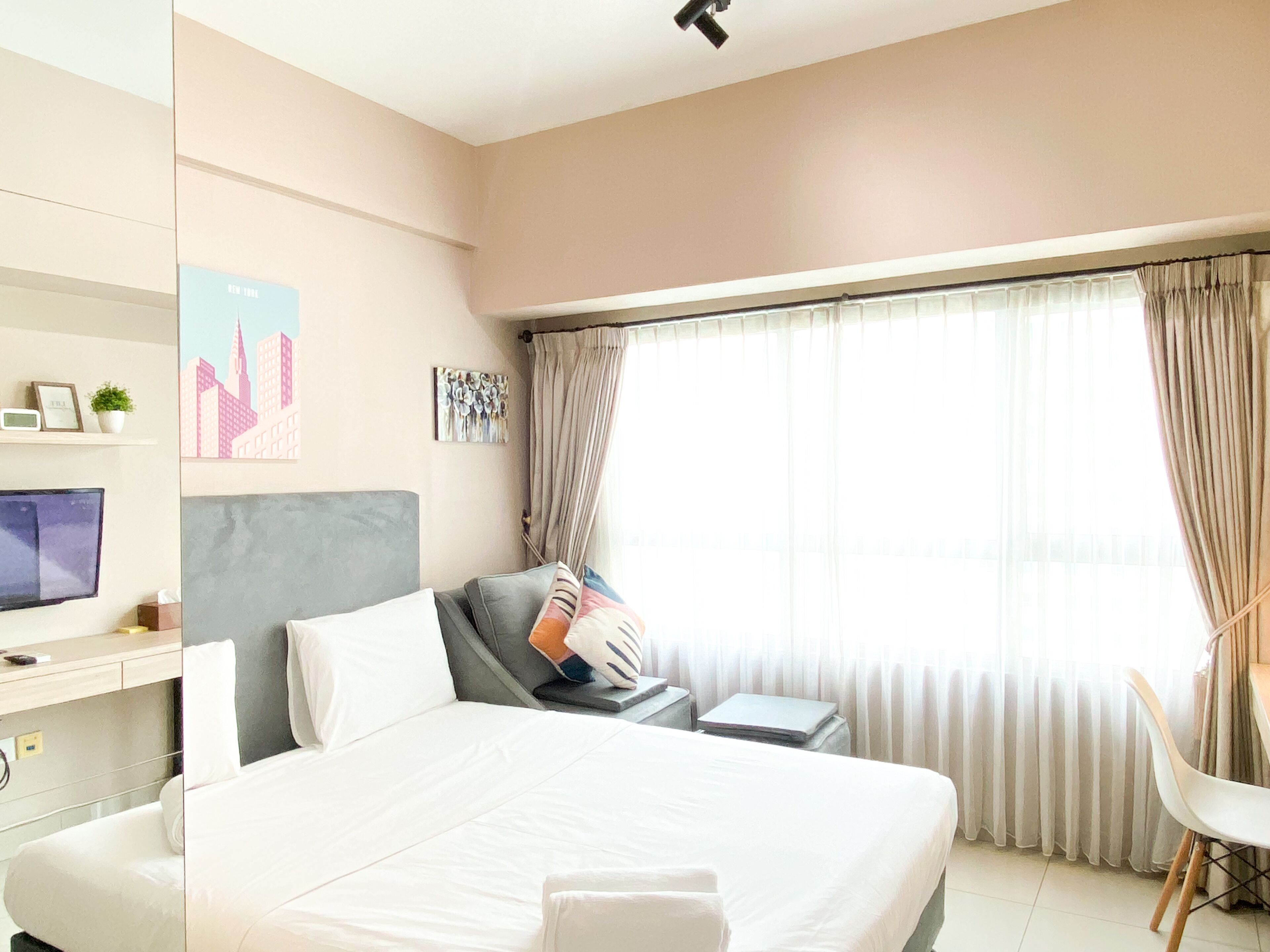 A hotel room with a bed, a desk, a chair, a TV, and a window with curtains.