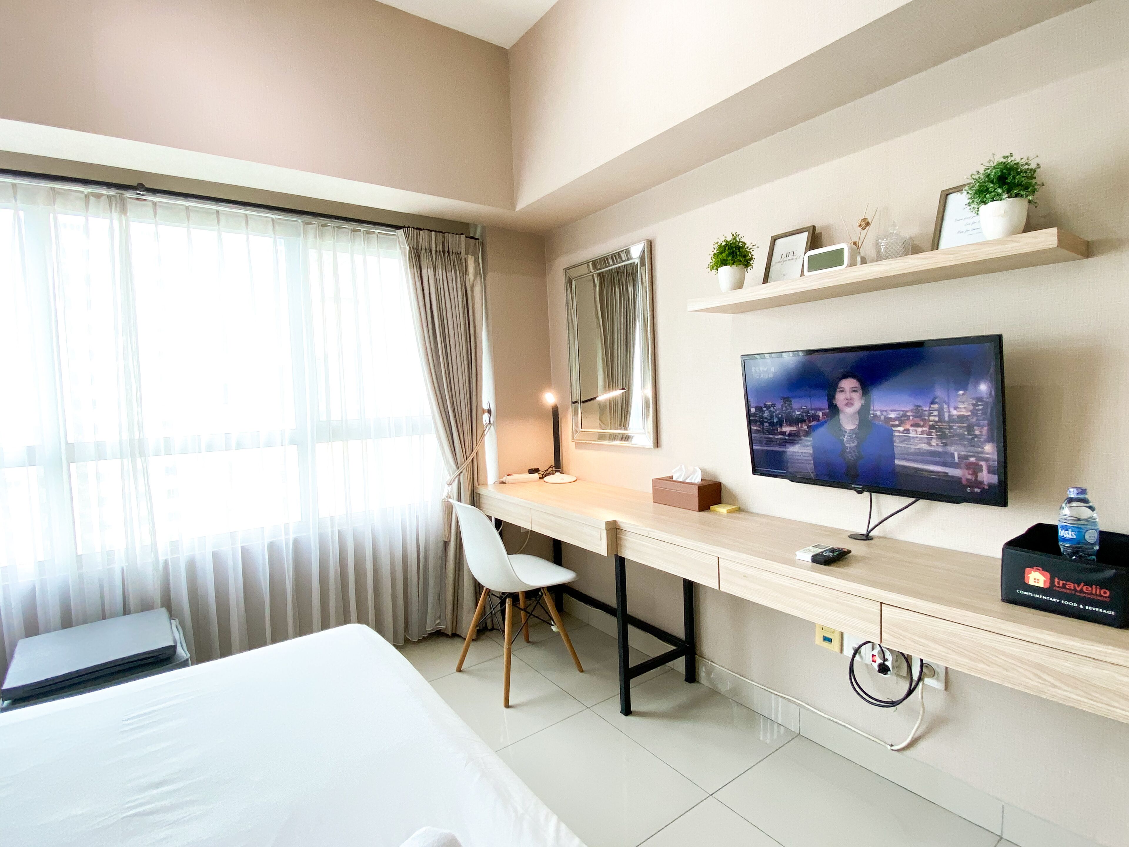 Une chambre d’hôtel avec un lit, un bureau et une chaise, une télévision et une fenêtre avec des rideaux.