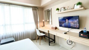Habitación de hotel con cama, escritorio, silla, televisor y ventana con cortinas.