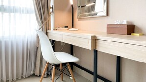 Una habitación de hotel moderna con un escritorio de madera, una silla blanca, un espejo y una mesita de noche con un dispensador de pañuelos y un objeto amarillo.
