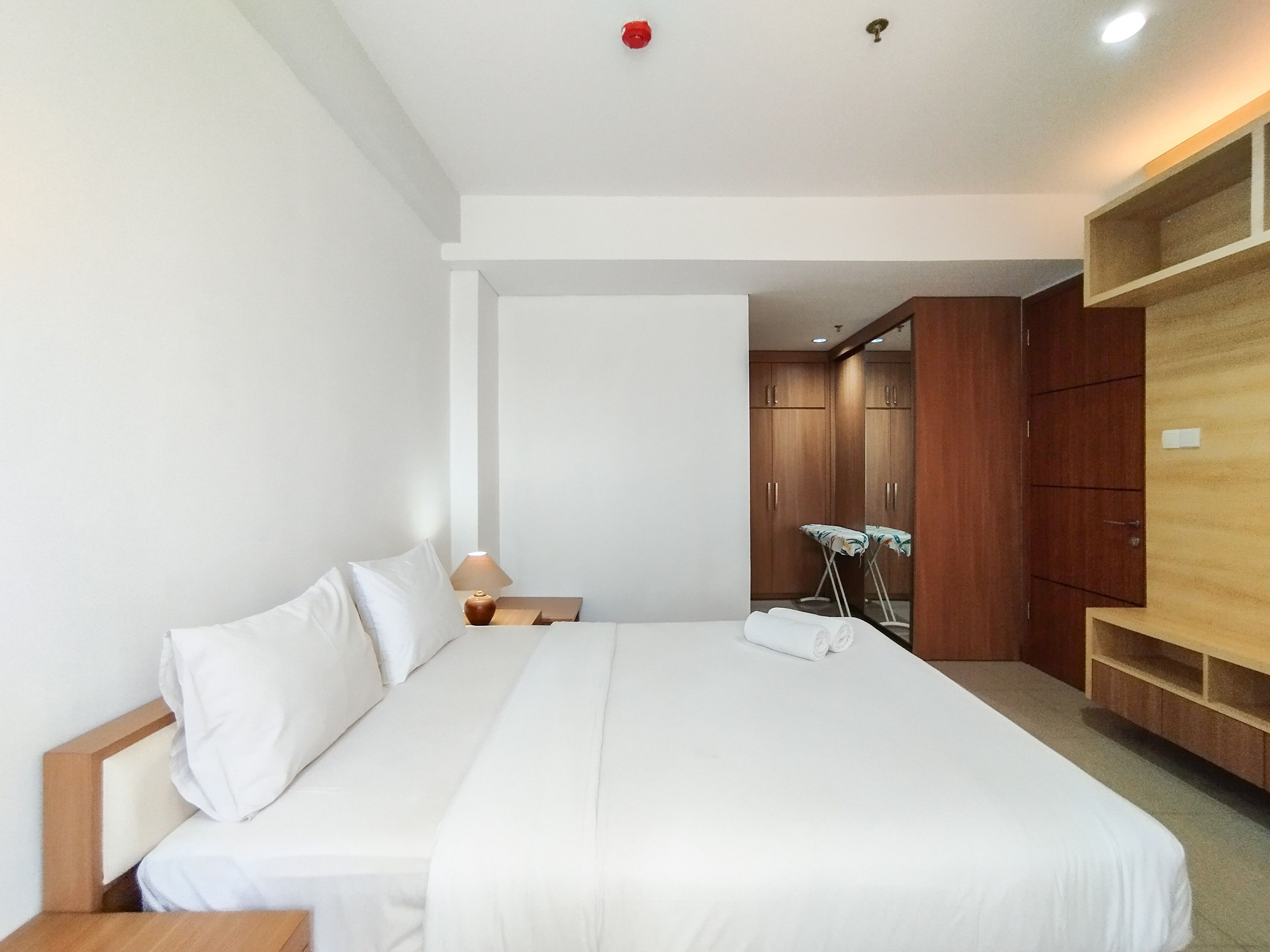 A hotel room with a large bed, wooden wardrobe, and a small table with a lamp.