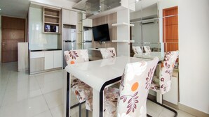 A modern dining area with a white table and floral-patterned chairs, a built-in TV, and a kitchen area with a refrigerator and microwave.