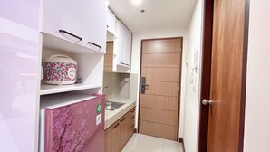 A compact kitchen with white cabinets, a pink appliance, and a wooden door. - Scenic Studio Room Apartment Vida View Makassar (Makassar)