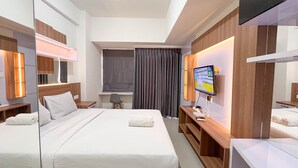 A hotel room with two beds, a desk, a chair, a TV, and a large mirror. - Scenic Studio Room Apartment Vida View Makassar (Makassar)