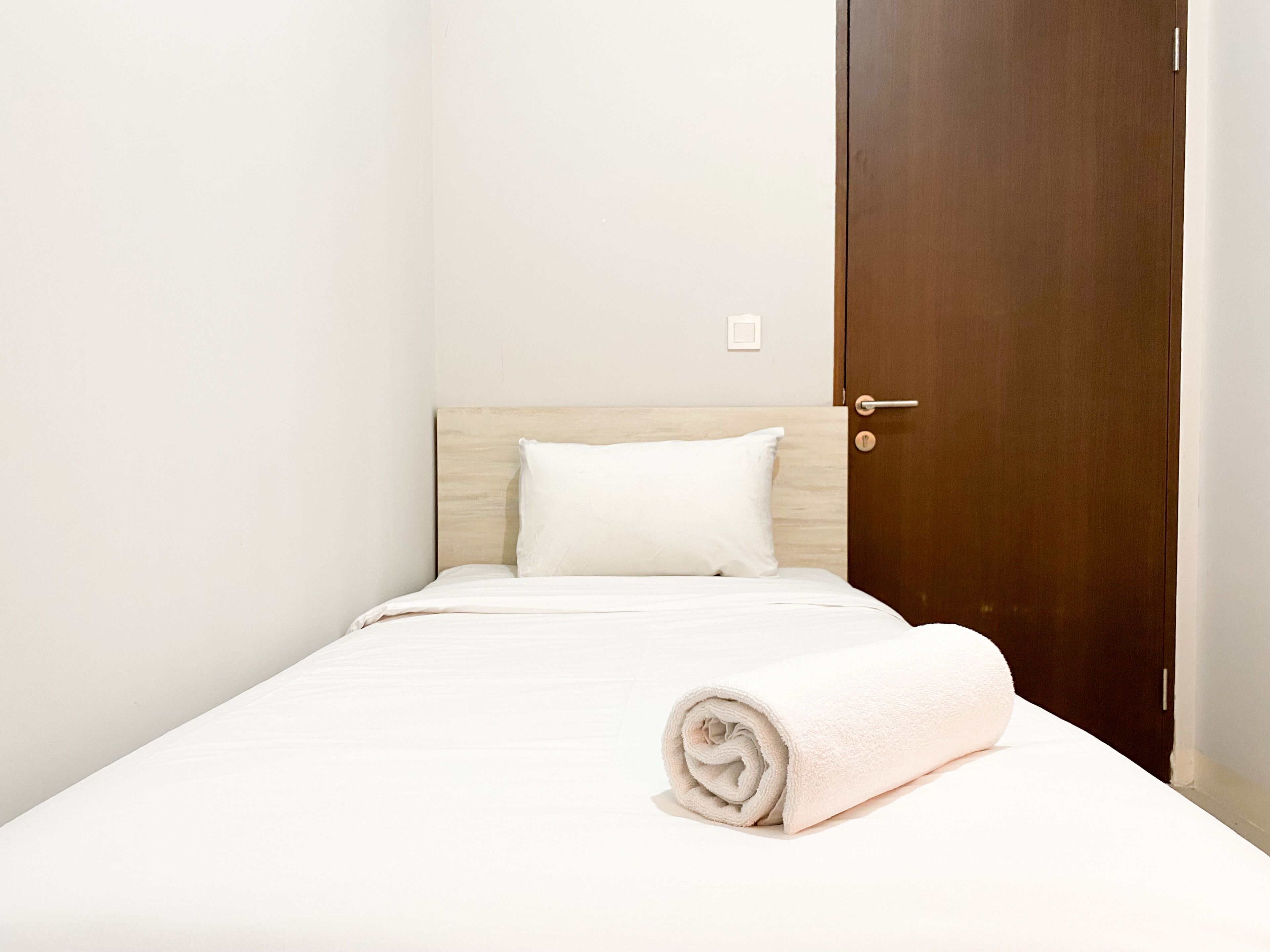 A neatly made bed with a white pillow and a rolled white towel.