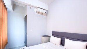 A hotel room with a bed, pillows, a bedside table, an air conditioning unit, and a door. - Comfort 2Br At Transpark Juanda Bekasi Timur Apartment (Bekasi)