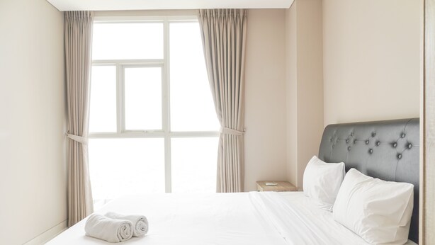 A hotel room with a neatly made bed, a window with curtains, and a bedside table.