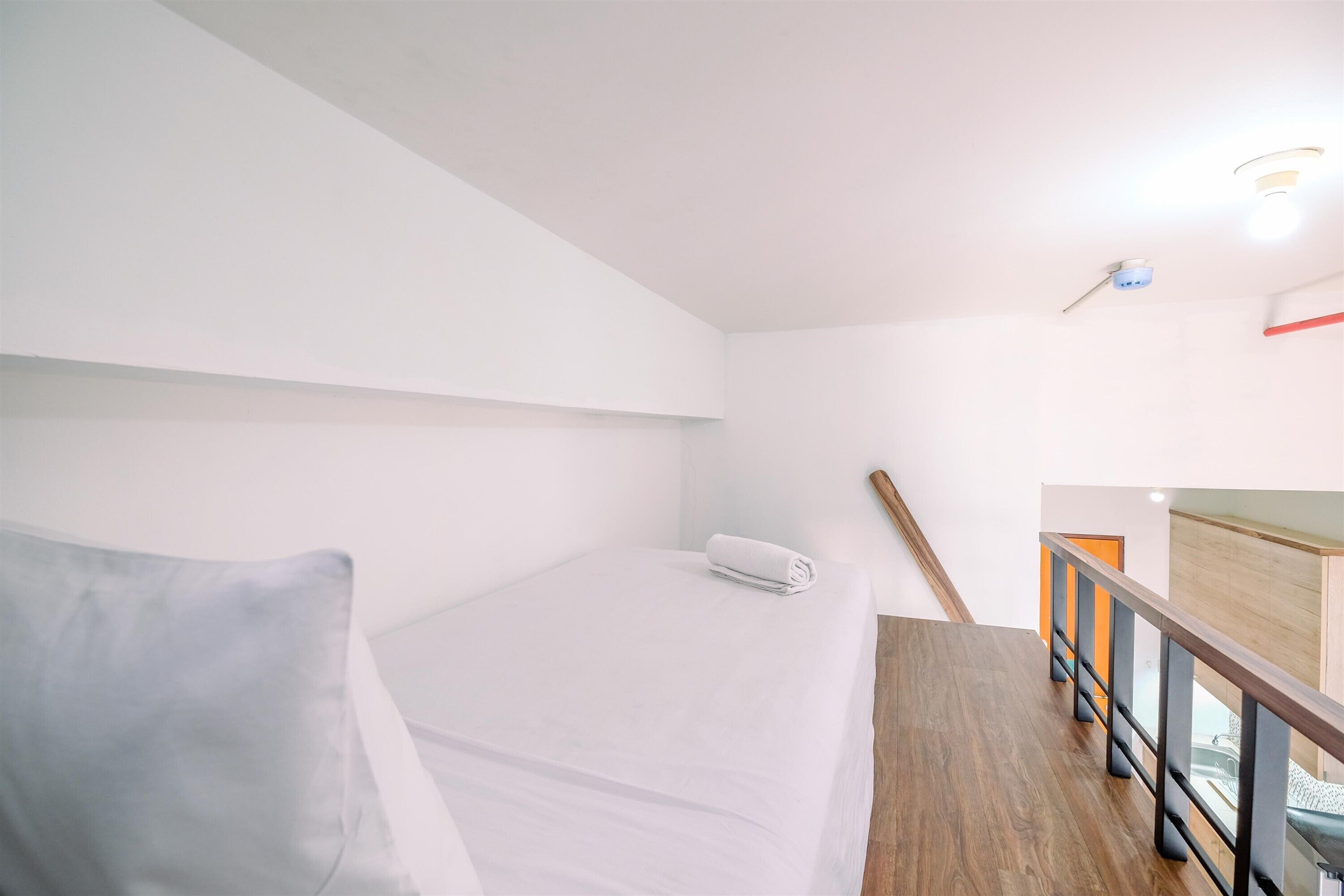A hotel room with a bed, a wooden floor, a railing, and a ceiling light.