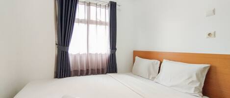 Una cama bien hecha con sábanas blancas, cabecera de madera y una ventana con cortinas de gasa.