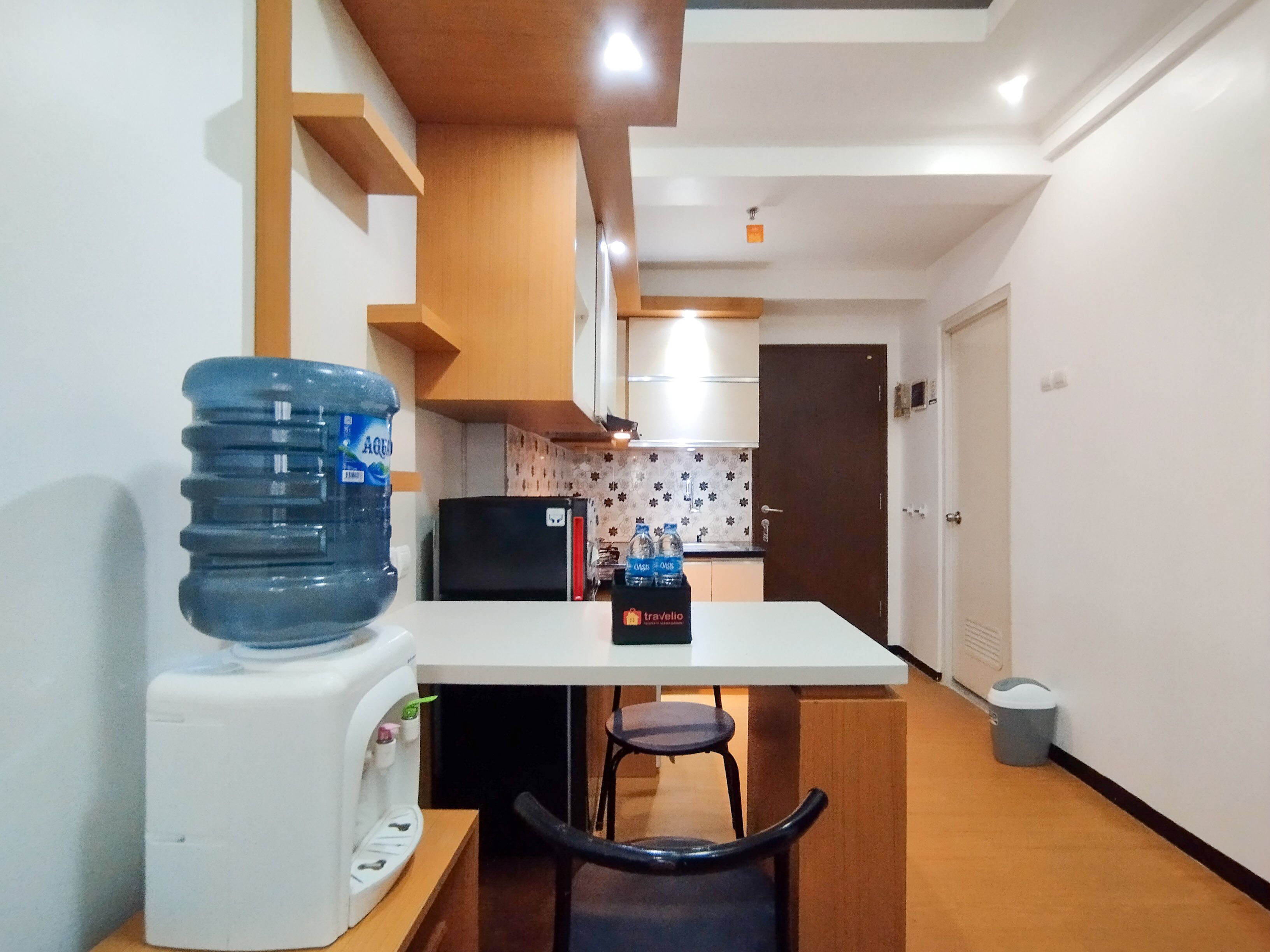 A compact kitchen with a white countertop, a water dispenser, a refrigerator, and a microwave.