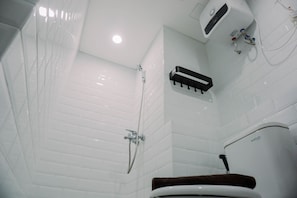 Um banheiro com paredes azulejadas em branco, chuveiro e vaso sanitário.
