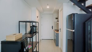 A compact kitchen with a black refrigerator, a wooden table with a box, and a metal shelf unit. - Comfortable And Homey Studio Loft At Kingland Avenue Apartment (South Tangerang)
