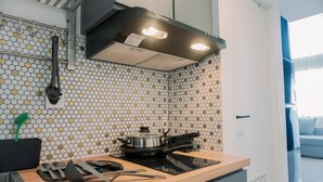 A modern kitchen with a black induction cooktop, a stainless steel pot, and a black spatula on the counter. - Comfortable And Homey Studio Loft At Kingland Avenue Apartment (South Tangerang)