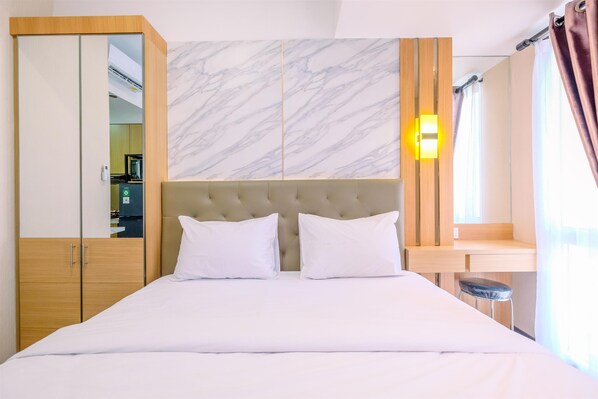 A hotel room with a bed, a wardrobe, a marble headboard, a nightstand, and a bathroom mirror. - Warm And Cozy Studio At Tokyo Riverside Pik 2 Apartment (Teluknaga)