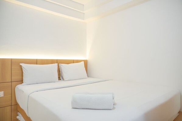 A neatly made bed with white linens and a folded towel, wooden headboard, and a clean, minimalist room design. - Good Choice And Minimalist 1Br Bassura City Apartment (Jakarta)